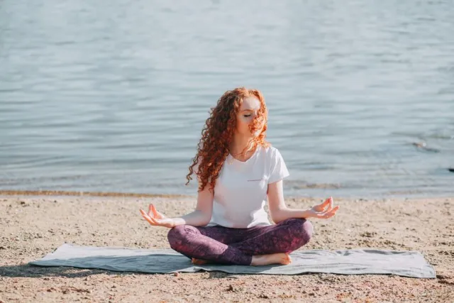 Mujer haciendo yoga sobre una esterilla junto al mar